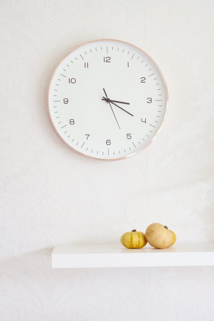 clock on a wall with a shelf and two small pumpkins on the shelf